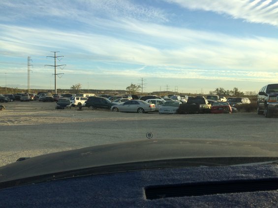 Junkyard scene with rows of parked cars under a cloudy sky, power lines in the distance