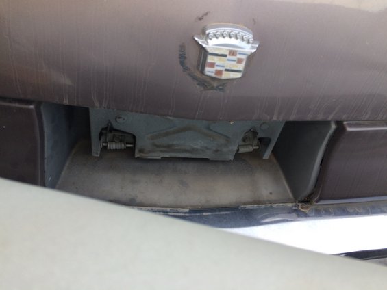 Brown car trunk with a chrome Cadillac crest emblem and visible latch mechanism below