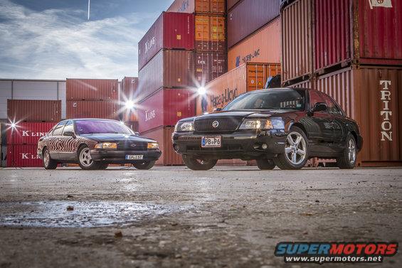 Black 2003 Mercury Marauder parked in front of shipping containers, with a dark sedan to its left