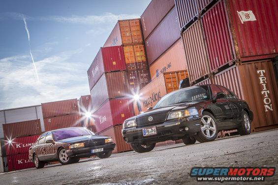 Black 2003 Mercury Marauder and a dark sedan parked in front of stacked shipping containers