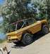 1971 Ford Bronco - A yellow 1971 Ford Bronco with a roll cage is parked on a dirt slope next to trees and water.