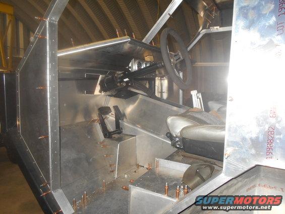 unfinished vehicle interior with steering wheel, pedals, and seats visible