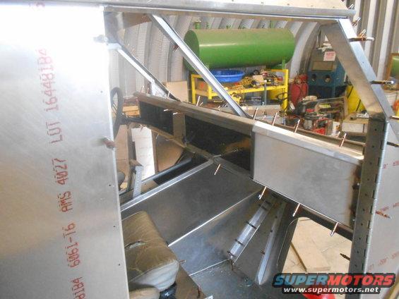Aluminum frame of a vehicle being built, with some seats visible. Text on the side reads 'AMS 4027 LOT 164481B4'