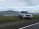 2003 Mercury Marauder - A silver sedan is parked on a grassy hill overlooking a town and rolling hills under a cloudy sky.