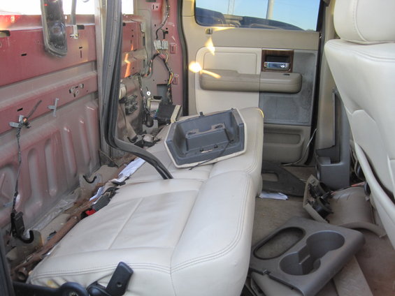 Interior of a pickup truck with seats and door panels removed, showing exposed wiring and structural components