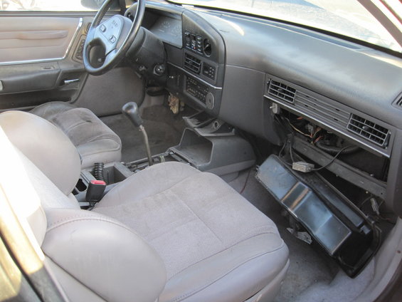 Car interior showing dashboard, steering wheel, and seats. Center console is partially disassembled