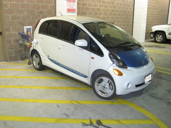 White and blue Mitsubishi i-MiEV electric car charging at a station