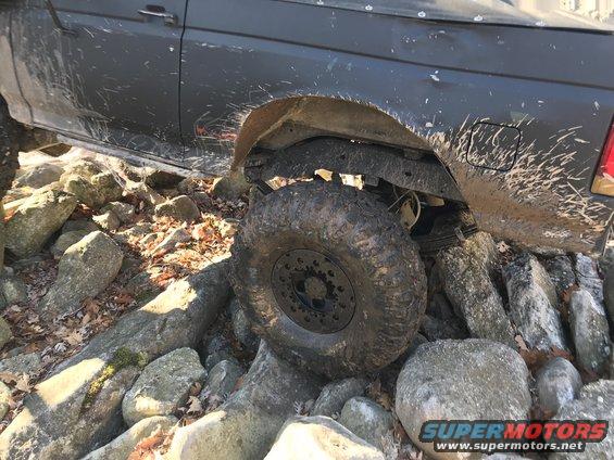 1989 Ford Bronco navigating rocky terrain, mud splattered on body