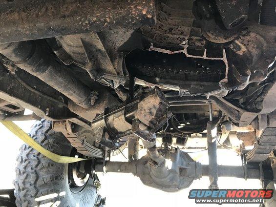 Underside view of a 4x4 with a damaged transmission or transfer case, leaf springs, and a spare tire visible