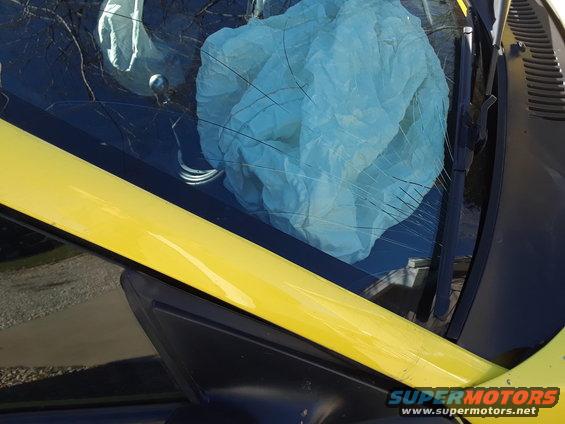 Yellow car interior with deployed airbag, cracked windshield, and Supermotors.net watermark