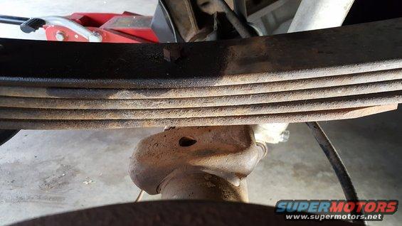 Rusty leaf springs above a differential housing with a red jack in the background