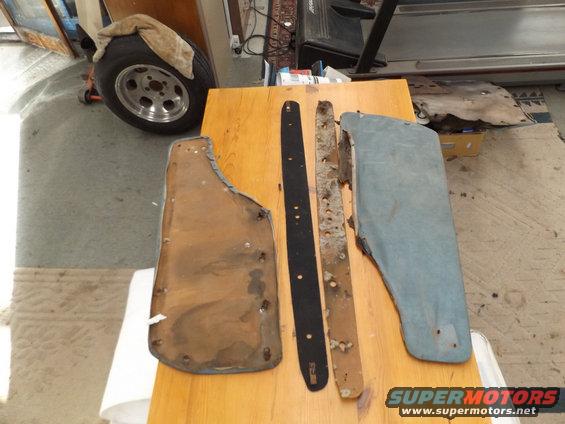 Car mud flaps and trim pieces laid out on a wooden table. A spare tire is visible in the background