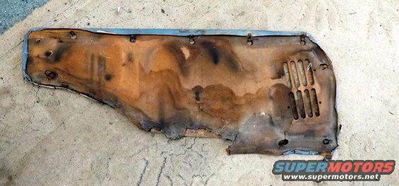 Worn automotive insulation panel with metal trim and vent holes, lying on a concrete surface