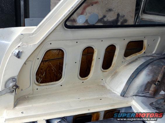 Interior panel of a car with multiple oval cutouts showing rust behind them. Some grey paint splotches on the window