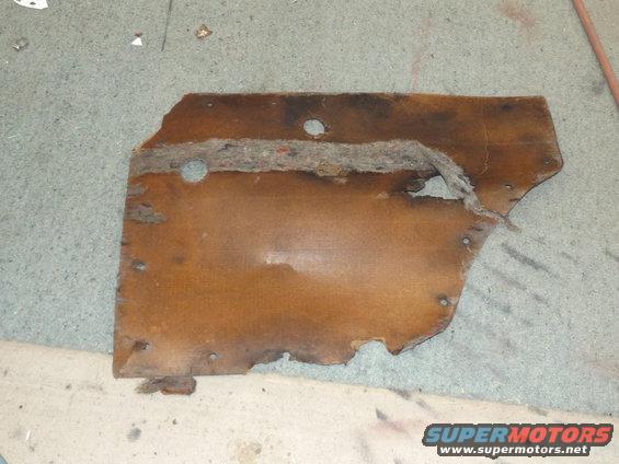 Worn brown door panel with frayed edges and holes, lying on a concrete floor