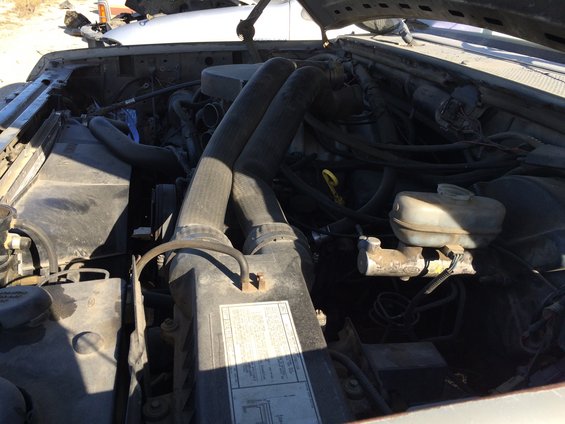 Engine bay with large hoses, brake fluid reservoir, and a sticker on the radiator cover