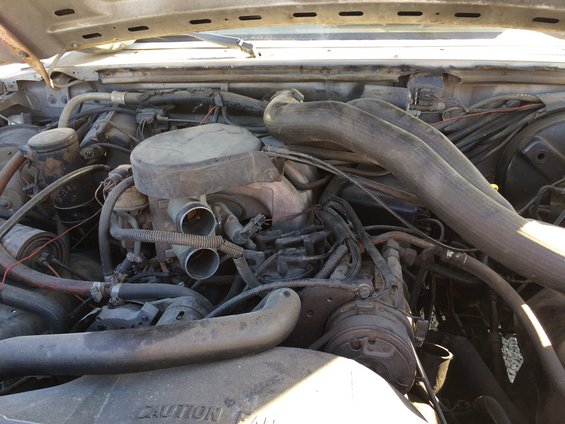 Engine bay with V8 engine, air intake, and hoses visible. Fan shroud has CAUTION text