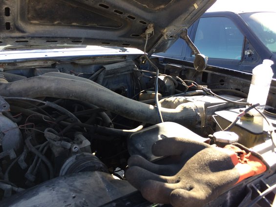 engine bay with hoses and wires visible, another vehicle in background