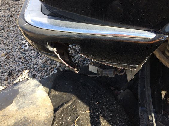 Close-up of a damaged black car bumper with chrome trim. Wires and connectors are exposed