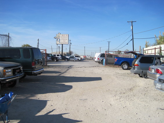 Junkyard with a sign for AL'S ATOMIC PICK U PART, multiple cars and vans parked on dirt lot under a clear blue sky