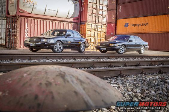 2003 Mercury Marauder and a Chevrolet Impala parked side-by-side on train tracks with shipping containers in the background