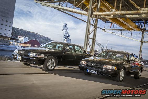 Black 2003 Mercury Marauder and a black Chevrolet sedan driving on a road near a harbor