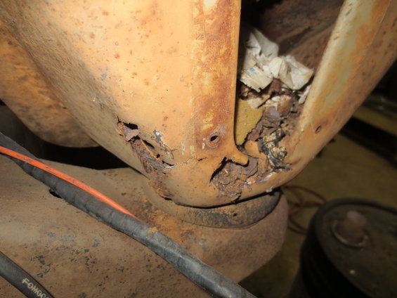 Close-up of heavily rusted metal on a vehicle frame, with some debris inside a cavity