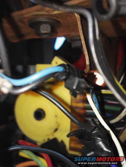 Close-up of a yellow plastic component with wires and a bolt in a vehicle's wiring harness