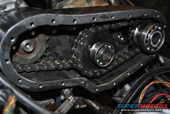Engine timing chain and sprockets within a metal casing, with visible bearings and wiring