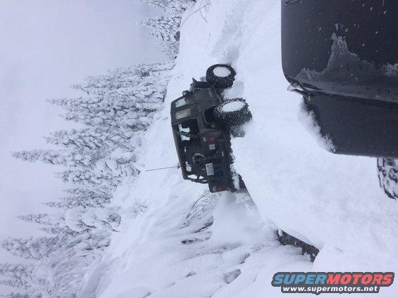 Off-road vehicle tipped over on a snowy slope next to a larger vehicle