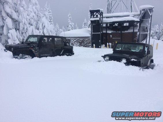 Two black Jeeps partially buried in snow, one a four-door model with 'Rubicon' visible
