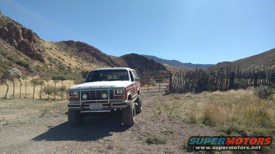 Ford Bronco parked on dirt road near a fence and hills