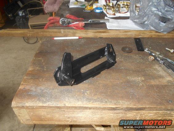 black metal bracket with a pivot point, resting on a wooden surface with tools nearby