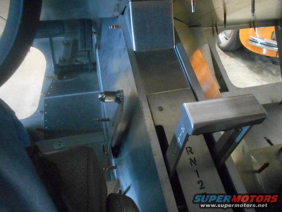 Vehicle interior showing a floor shifter with R, N, 1, 2 markings. A partial orange vehicle is visible in the background