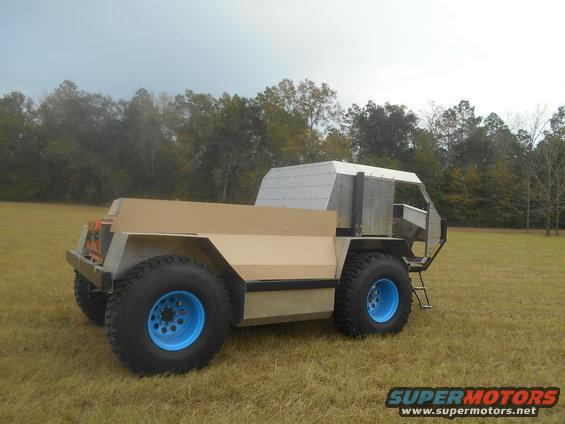 Custom off-road vehicle with large blue wheels and a tan body, viewed from the front-right