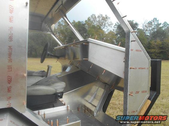 unfinished interior of a vehicle with exposed metal framing, a steering wheel, and a seat