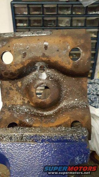 rusted metal bracket held in a blue vise, with metal shavings around it. A toolbox is in the background