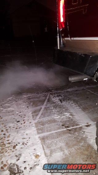 Rear of a vehicle with exhaust smoke coming from the tailpipe onto a snowy ground