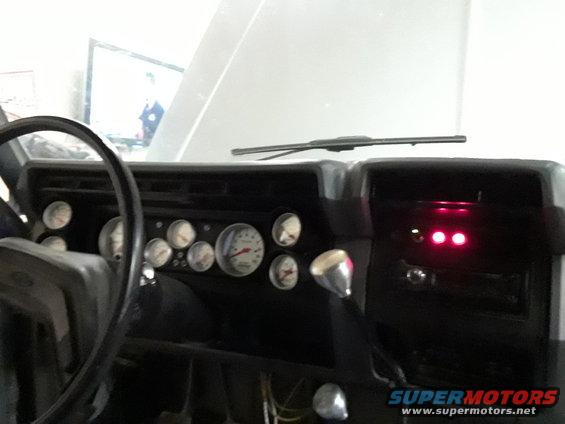 Dashboard interior with multiple gauges and a chrome shifter. Two red indicator lights are illuminated