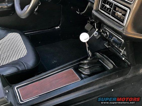 Interior shot of a car's center console with a Hurst shifter, woodgrain trim, and houndstooth seat
