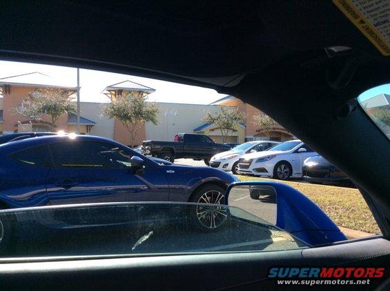 Blue coupe parked in a lot, side view. Other cars and a truck are visible
