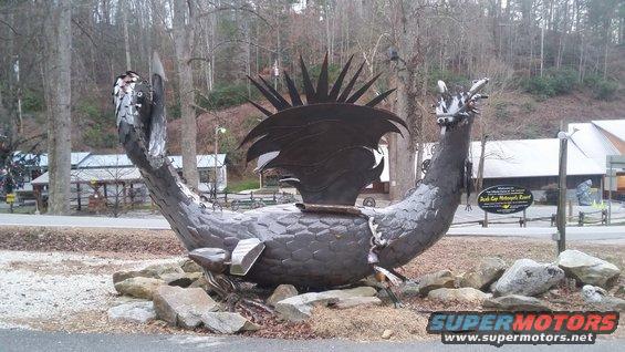 Metal dragon sculpture with spiky head crest, lying on rocks
