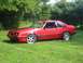 1986 Ford Mustang - Side view of a red 1986 Ford Mustang GT coupe parked on a grassy lawn.