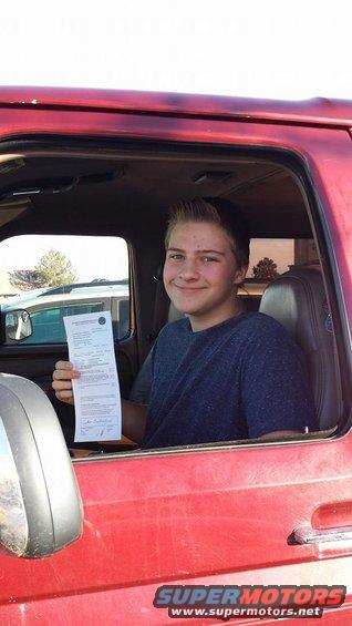 Young man in a red Ford Bronco holding a document.