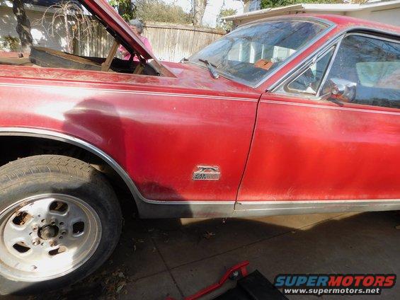 Red 1968 Mercury Cougar side view, hood open, showing engine bay. Chrome trim and fender emblem visible