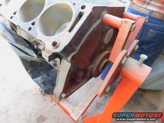 Engine block on orange stand, showing cylinder bores and mounting hardware