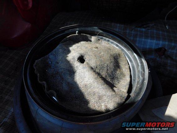 Spare tire well with a gray mat and a hole in it