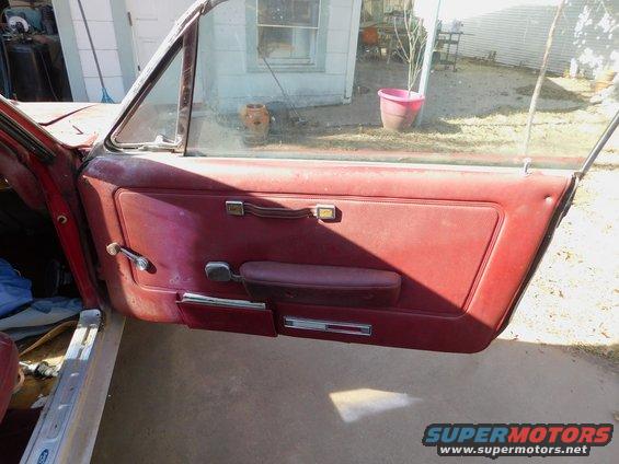 Interior of a red car door showing the armrest, window crank, and door handle