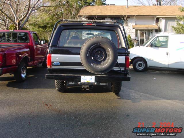 1995 Ford Bronco rear view with spare tire, parked next to a red pickup truck and a white van