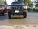 1995 Ford Bronco - Two Ford trucks are parked on a wet asphalt surface in a residential area.